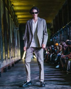 A man wearing a grey suit and black brogues catwalking.