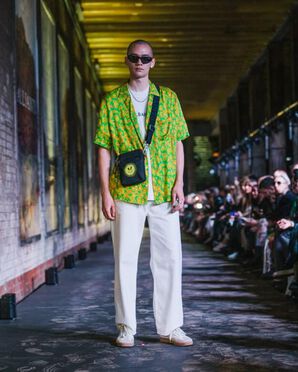 A man wearing a neon green short sleeve shirt over a t-shirt and white wide leg trousers catwalking.