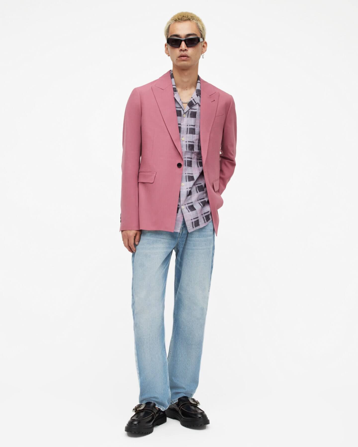 Man wearing a pink blazer over checked shirt and light blue jeans.