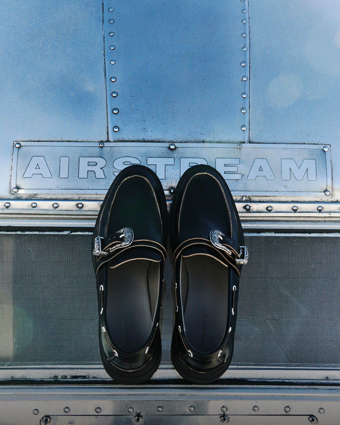 Two black leather loafers with ornate silver buckles resting on an airplane.