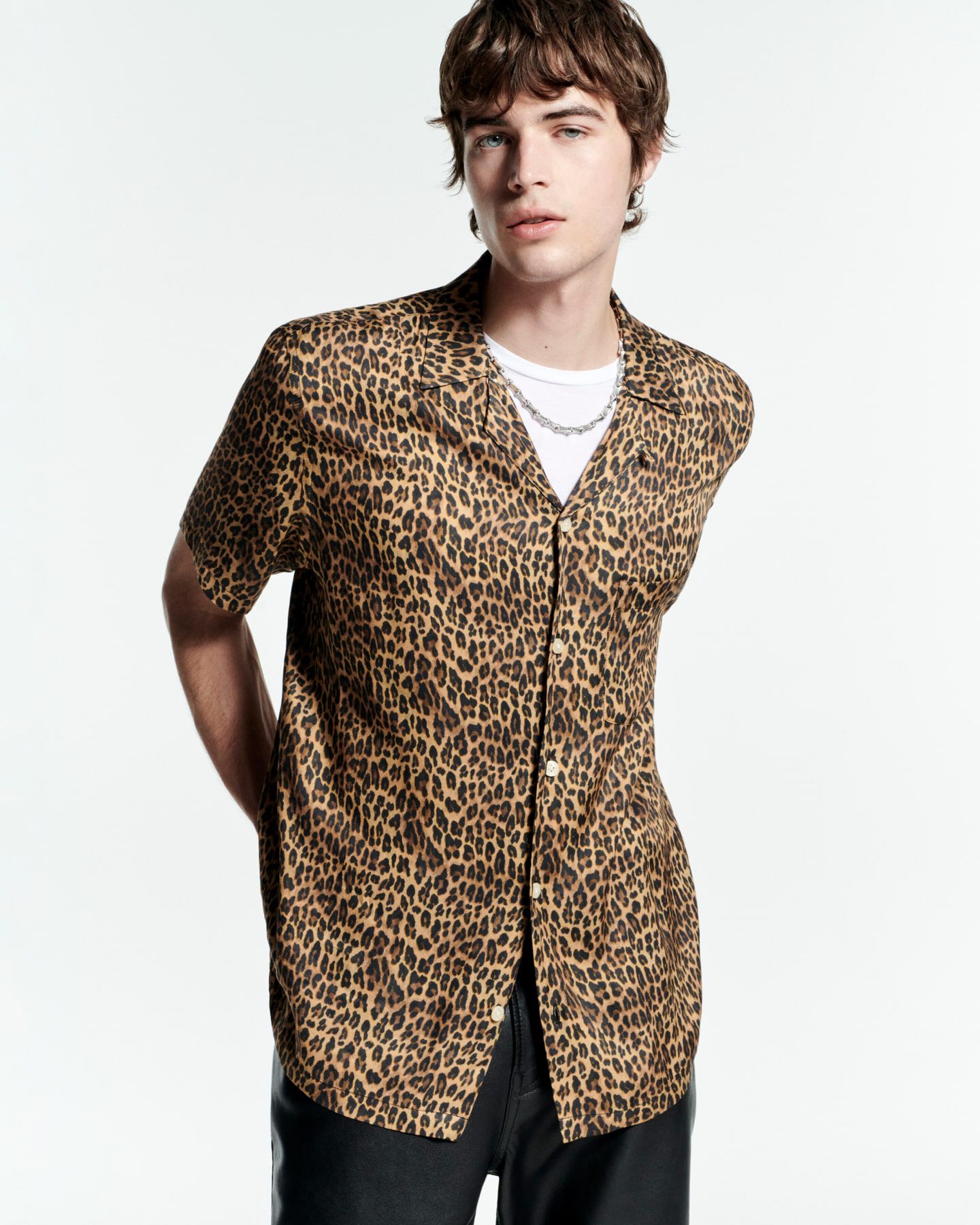 A man wearing a leopard print short sleeved shirt and black trousers.