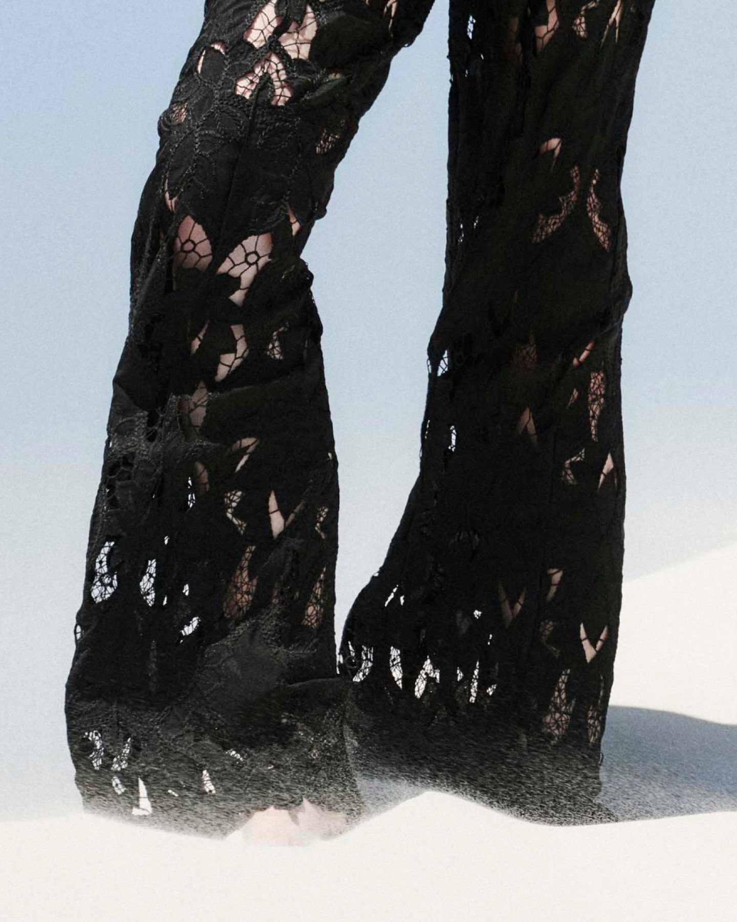 Closeup of floral lace cutout black trousers in the desert, in front of a blue sky.