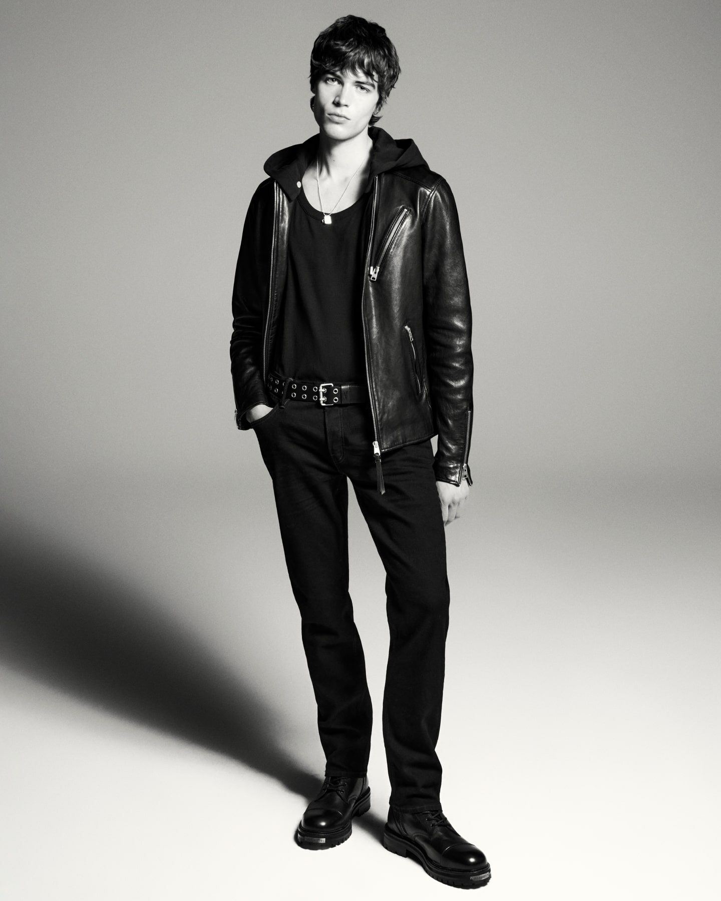 A black and white image of a man wearing leather jacket and jeans.