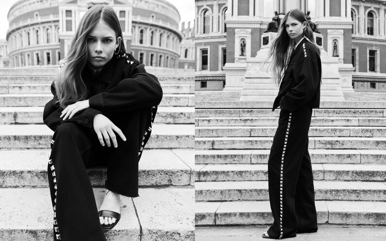 A black and white image of a model standing on steps wearing a black blazer and trousers.