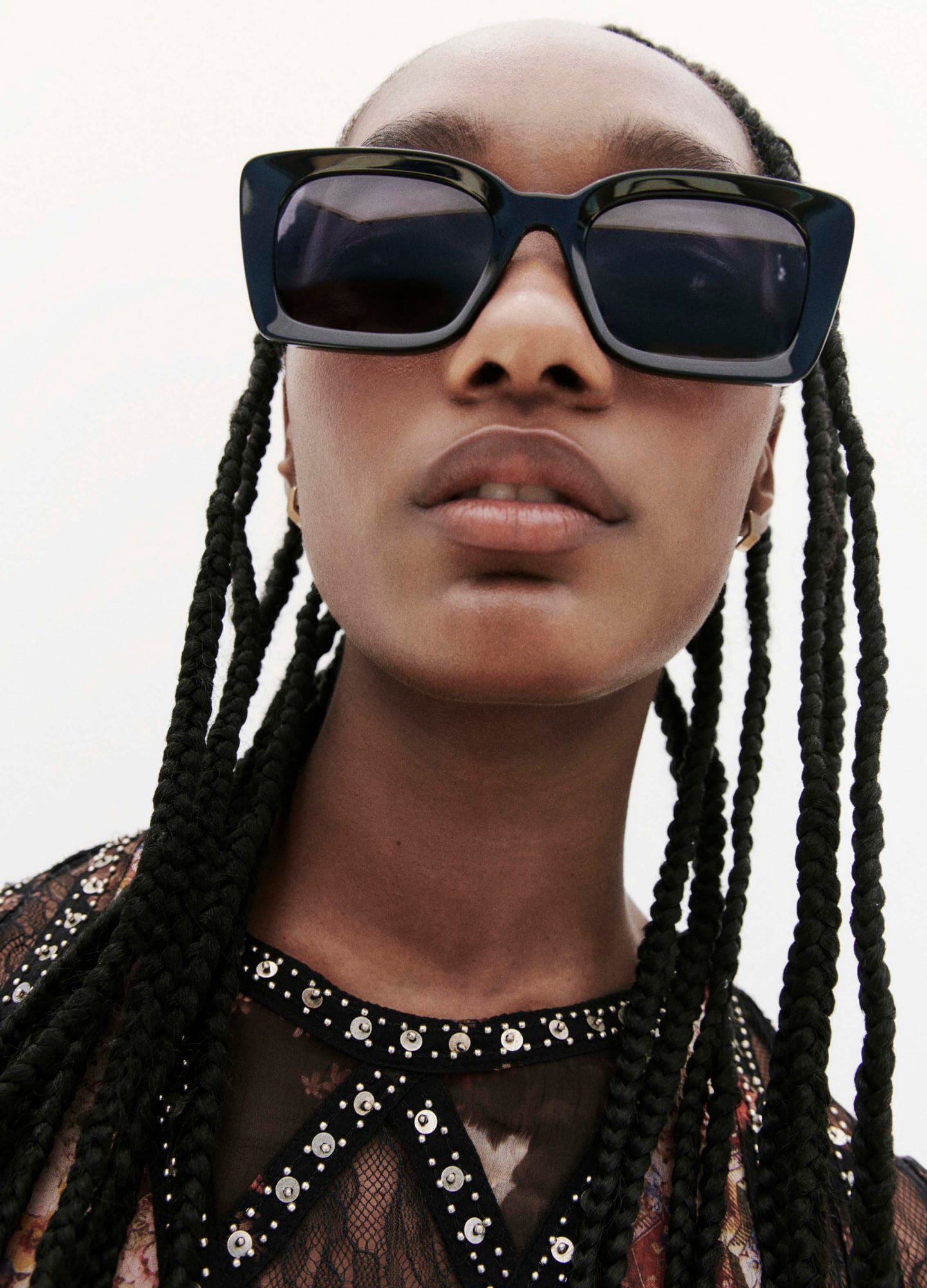 Closeup of a female model wearing a printed dress with panels and ornate trims and black sunglasses.